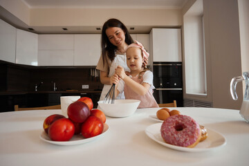 Family in the kitchen. Beautiful mother with her little daughter. A woman in an apron is kneading. Girl learning to cook dough