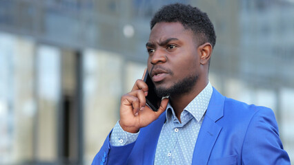 African American man has call with colleague on black smartphone. Bearded businessman talks on...