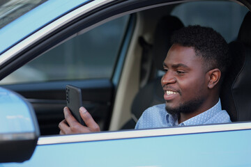 African American driver with phone sitting at car steering wheel. Bearded man spends time in traffic jams communicating with friends.