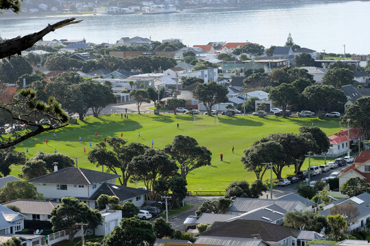 Local football game with players on the pitch surrounded by residential houses and a glimpse of ocean in the background in the suburb of Seatoun, Wellington, New Zealand Aotearoa