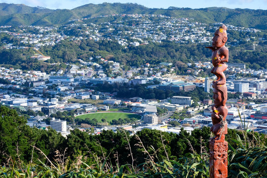 A māori pou intricate cultural sculpture in Capital city Wellington with residential houses on the hills in New Zealand Aotearoa