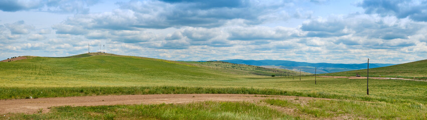 Obraz premium Bald Mountain in the Buryat Republic of Russia. Green hills against a blue sky with clouds.