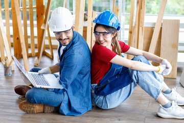 Asian professional female and Indian bearded male engineer architect foreman labor worker wear safety goggles and gloves sitting on floor smiling working with laptop computer discussing together