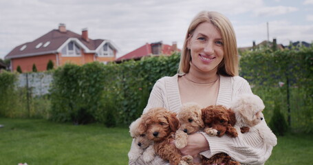 Portrait of a happy woman holding five maltipoo puppies in her hands