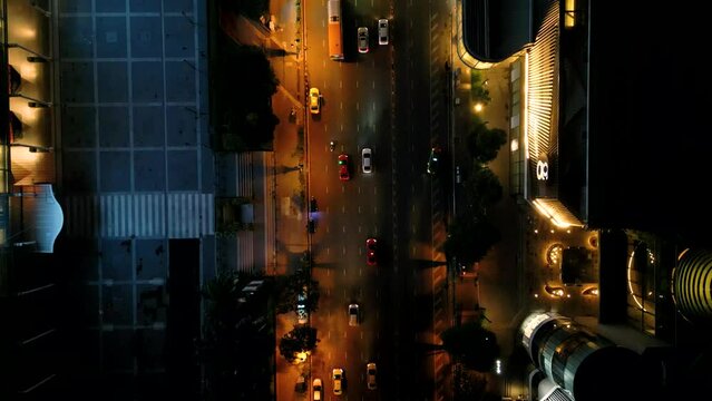4K Cinematic urban drone footage of an aerial view of cars driving on the road with the drone looking down at 90 degrees, in the middle of downtown Bangkok, Thailand at night.