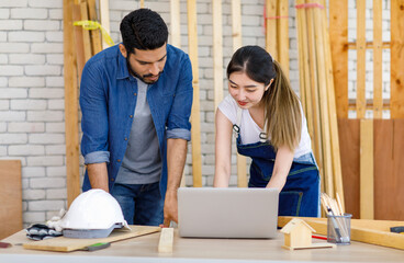 Asian professional cheerful female engineer architect foreman labor worker sitting smiling holding tablet computer discussing with Indian bearded male carpenter in workshop housing construction site