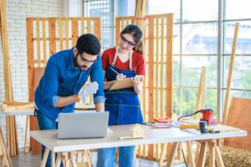 Indian professional male engineer foreman labor worker using laptop computer meeting discussing with cheerful female colleague wear safety goggles writing note on paper clipboard in construction site