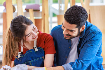 Fototapeta premium Asian professional female and Indian bearded male engineer architect foreman labor worker wear safety goggles and gloves sitting cuddling leaning together smiling working via laptop notebook computer
