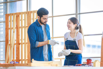 Asian professional cheerful female engineer architect foreman labor worker sitting smiling holding tablet computer discussing with Indian bearded male carpenter in workshop housing construction site