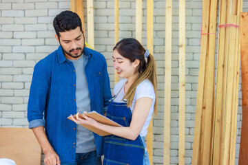 Asian professional cheerful female engineer architect foreman labor worker standing smiling holding tablet computer discussing with Indian bearded male carpenter in workshop housing construction site