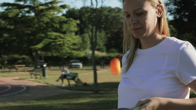 a girl of European appearance with blond hair, in a white T-shirt plays ping pong, fills a ball with a racket in the park.