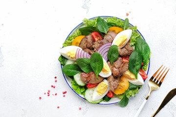 Perigord salad with chicken liver, tomatoes, cucumbers, eggs, lettuce and spinach. Black kitchen table background, top view
