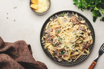 Mushroom Tagliatelle Pasta with parmesan cheese and cream sauce on white background, top view. Prepared italian pasta with champignon on gray plate