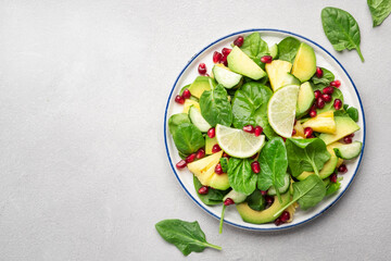 Fresh vegan salad with pineapple, spinach, avocado and pomegranate seeds, gray kitchen table, top view. Healthy eating, clean food, diet, weight loss concept
