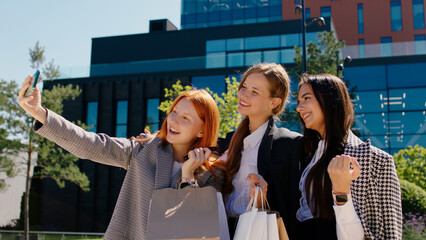 In front of the camera group of young women after their work day taking some selfies with smartphone beside of amazing modern business building