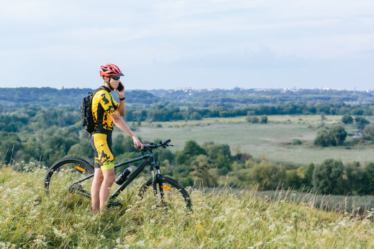 Happy male cyclist sending a text message on his mobile phone. Image of a cyclist on a mountain bike using a smartphone navigator exploring a map and searching for GPS coordinates while cycling.