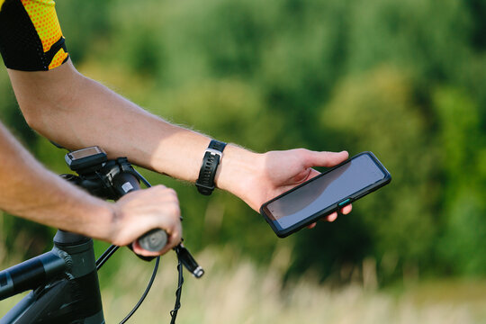 Happy male cyclist sending a text message on his mobile phone. Image of a cyclist on a mountain bike using a smartphone navigator exploring a map and searching for GPS coordinates while cycling.