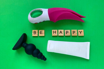 Sex toys and inscription BE HAPPY. Vibrator, lubricant and butt plug on green background. Useful...