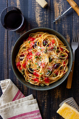 Spaghetti pasta Alla Puttanesca with capers, Kalamata olives, cheese, tomatoes and anchovies. Italian food.