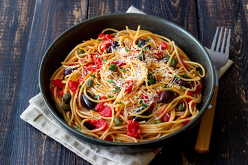 Spaghetti pasta Alla Puttanesca with capers, Kalamata olives, cheese, tomatoes and anchovies. Italian food.