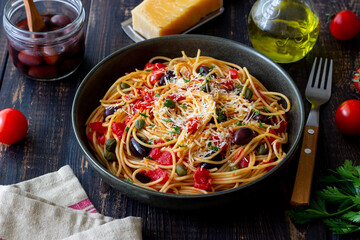 Spaghetti pasta Alla Puttanesca with capers, Kalamata olives, cheese, tomatoes and anchovies. Italian food.