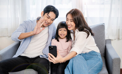 Portrait of happy asian family with toddler girl child use smartphone selfie say hi virtual in living room. Happy live online influencer blogger. Technology connected people family lifestyle concept