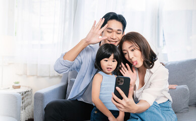 Portrait of happy asian family with toddler girl child use smartphone selfie say hi virtual in...