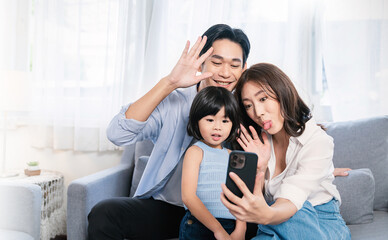 Portrait of happy asian family with toddler girl child use smartphone selfie say hi virtual in living room. Happy live online influencer blogger. Technology connected people family lifestyle concept