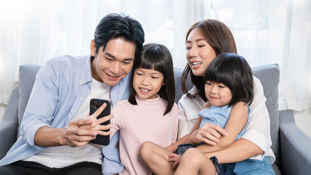 Portrait of happy asian family with toddler girl child use smartphone selfie say hi virtual in living room. Happy live online influencer blogger. Technology connected people family lifestyle concept