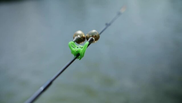 Silver fishing bells are worn on a fishing rod while fishing. Bite-call signal, at the tip of the rod. A bite alarm will alert you to a bite. Fishing tackle close-up.