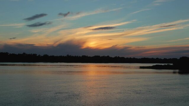 Sunset over the river with cirrus clouds. Clouds fly across the sky from left to right. Water in Dnieper River flows from right to left. There is a forest on the horizon. Nature of Ukraine. Timelapse