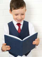 Positive elementary school nerd student holding an open textbook and looking into a book on a light...