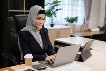 Young Arabic female entrepreneur wearing a hijab working online with a laptop at modern office