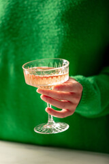 Female hand hold glass of wine. Woman in green swea