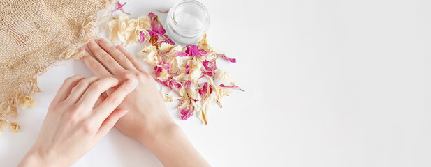 woman applies moisturizer to her hands on a white background with dry flower petals