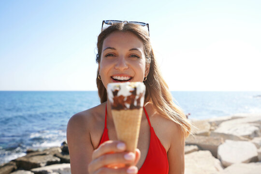 Close-up of beautiful bikini woman holding ice cream cone italian gelato looking to the camera on the beach on summer
