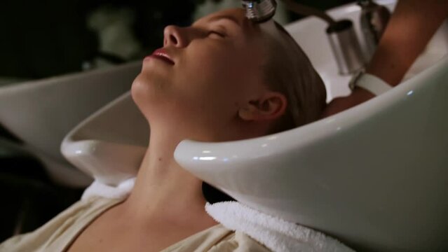  young woman lying down on salon washing bed getting hair washed by professional stylist. Beautiful customer feeling relax and happy while hairdresser massaging at beauty salon or barber shop.