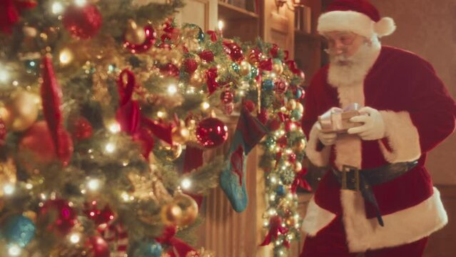 Medium slowmo of Santa Claus crawling to beautifully decorated fireplace and putting Christmas present box into stocking on Christmas Eve