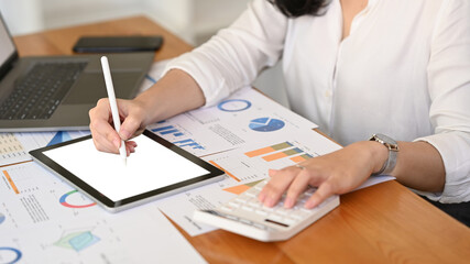 Professional businesswoman analyzing stock charts, using digital tablet on wooden office desk
