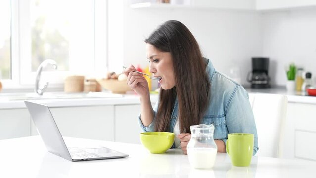 Positive lady sit kitchen lady have web conversation netbook eat wheat snack