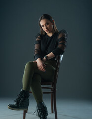 attractive brunette model sitting on a old chair posing and looking at camera on grey background