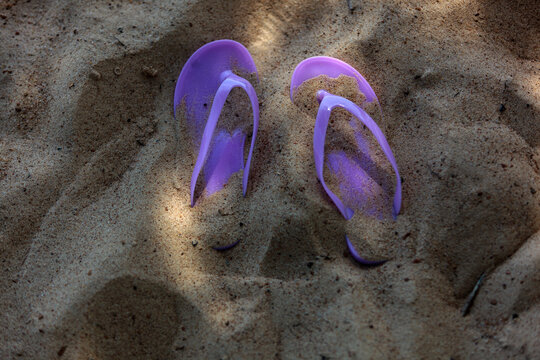 Purple sandals covered with beach sand with a glimmer of light.