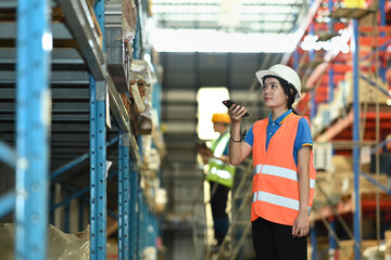 Female warehouse worker checking inventory boxes with barcode scanner on shelf in a large warehouse