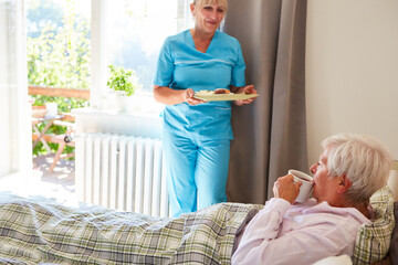 Altenpflegerin bringt einer Seniorin das Frühstück ans Bett