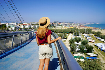 Beautiful woman walking on Pescara modern bridge enjoying seascape from promenade in Abruzzo...