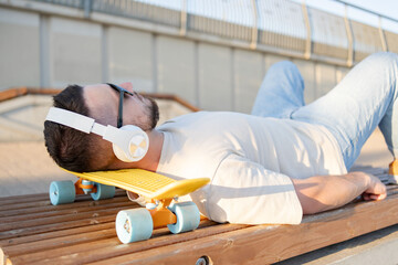 Attractive man relaxing with music and a skateboard. Guy relaxing in the skate park.