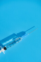 A disposable syringe with a metal needle casts a shadow on a blue background. Top view, place for text.
