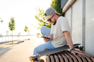 Happy young  man with skateboard looking at mobile phone social media app to connect with friends. Urban lifestyle, street fashion and technology concept