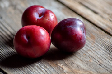 Close-up of three ripe plums on rustic wood