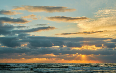Sunset over the sea with colorful clouds, orange sunlight, the rays of the sun shine through the clouds. The idea of a background or splash screen.